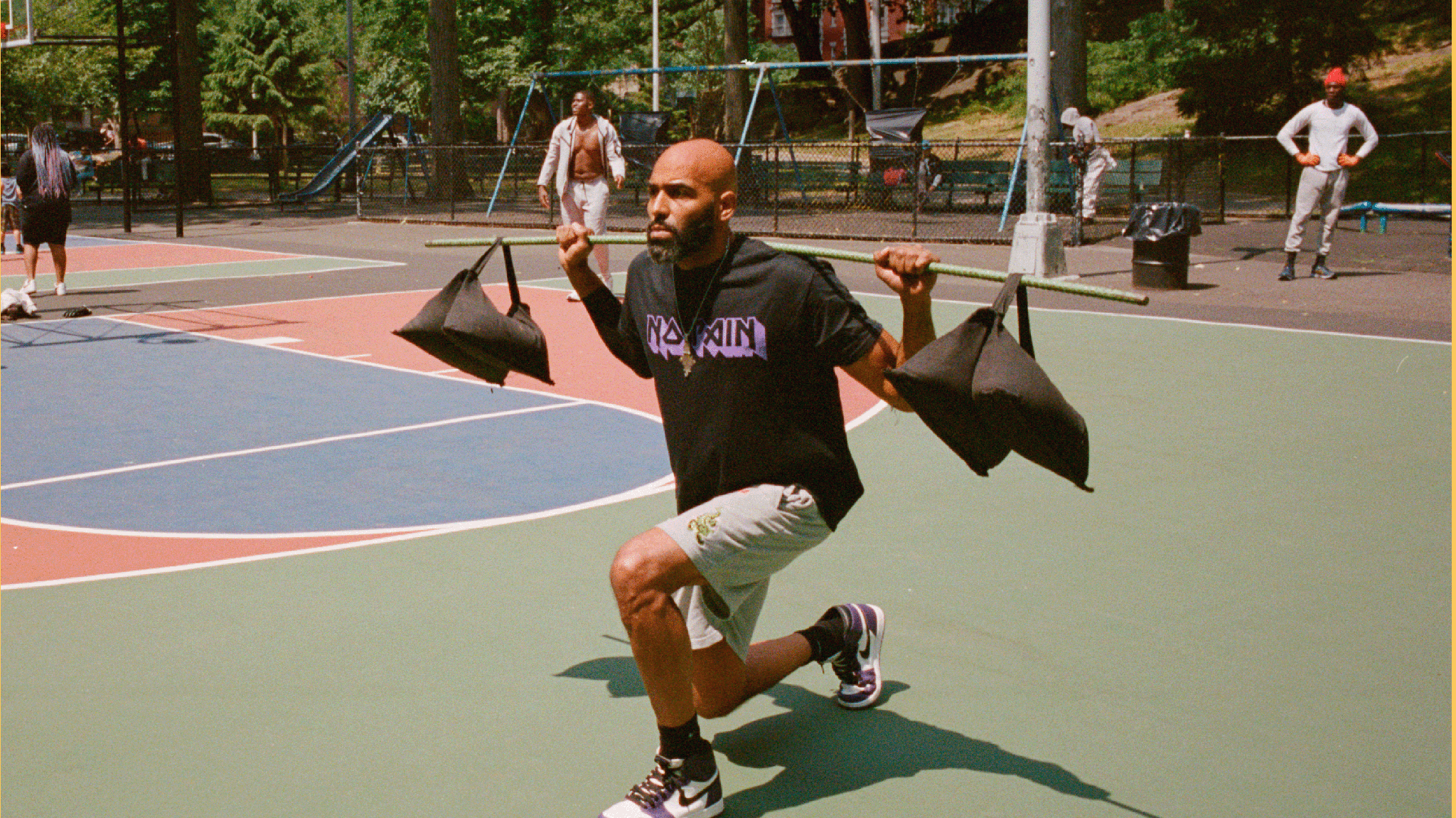 Man doing lunges in a basketball court while carrying a bar with weights on shoulders.